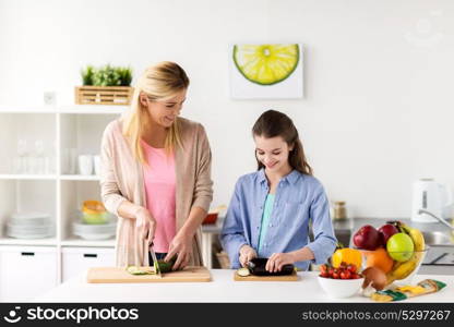 cooking food, healthy eating, family and people concept - happy mother and daughter chopping vegetables for dinner at home kitchen. happy family cooking dinner at home kitchen