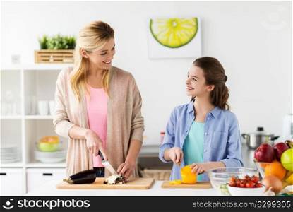 cooking food, healthy eating, family and people concept - happy mother and daughter chopping vegetables for dinner at home kitchen. happy family cooking dinner at home kitchen