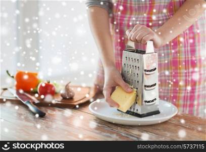 cooking, food, people and home concept - close up of female hands with grater and vegetables grating cheese in kitchen