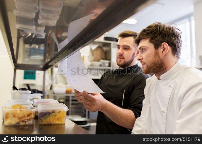 cooking food, profession and people concept - happy male chef and cook with grocery lists or bills at restaurant kitchen. chef and cook with lists or bills at kitchen
