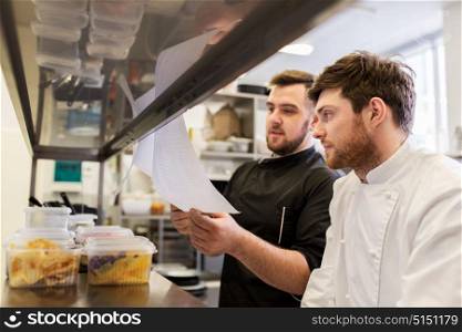 cooking food, profession and people concept - happy male chef and cook with grocery lists or bills at restaurant kitchen. chef and cook with lists or bills at kitchen