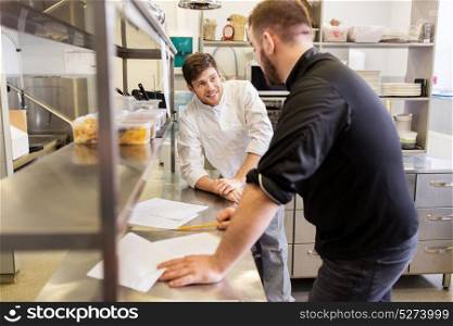 cooking food, profession and people concept - happy male chef and cook with grocery lists or bills at restaurant kitchen. chef and cook with grocery list at kitchen