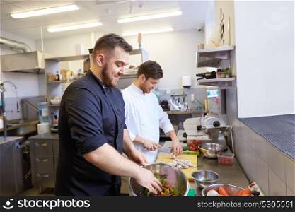 cooking food, profession and people concept - happy male chef and cook with knife chopping champignons and making salad at restaurant kitchen. chef and cook cooking food at restaurant kitchen