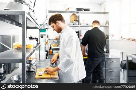 cooking food, profession and people concept - happy male chef and cook with knife chopping champignons on cutting board at restaurant kitchen. chef and cook cooking food at restaurant kitchen