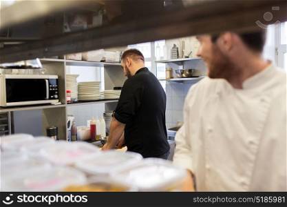 cooking food, profession and people concept - happy male chef and cook at restaurant kitchen. chef and cook cooking food at restaurant kitchen
