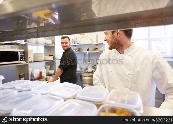 cooking food, profession and people concept - happy male chef and cook at restaurant kitchen. chef and cook cooking food at restaurant kitchen