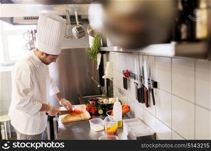 cooking food, profession and people concept - happy male chef cook with knife chopping tomatoes on cutting board at restaurant kitchen. happy male chef cooking food at restaurant kitchen