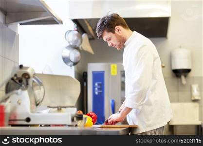 cooking food, profession and people concept - happy male chef cook with knife chopping paprika on cutting board at restaurant kitchen. happy male chef cooking food at restaurant kitchen