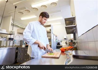 cooking food, profession and people concept - happy male chef cook with knife chopping celery on cutting board at restaurant kitchen. happy male chef cooking food at restaurant kitchen