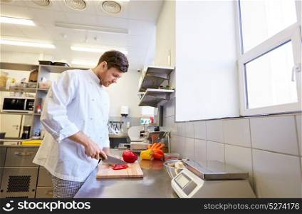 cooking food, profession and people concept - happy male chef cook with knife chopping paprika on cutting board at restaurant kitchen. happy male chef cooking food at restaurant kitchen