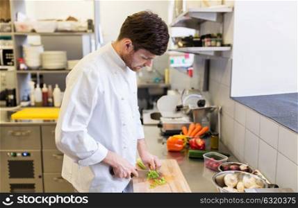 cooking food, profession and people concept - happy male chef cook with knife chopping celery on cutting board at restaurant kitchen. happy male chef cooking food at restaurant kitchen