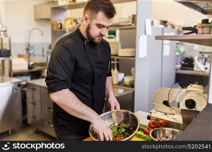 cooking food, profession and people concept - male chef cook making salad at restaurant kitchen. chef cook making food at restaurant kitchen