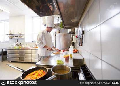 cooking food, profession and people concept - male chef cook with knife chopping tomatoes on cutting board at restaurant kitchen. male chef cooking food at restaurant kitchen