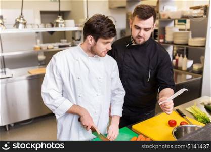 cooking food, profession and people concept - two happy male chefs looking to order or recipe at restaurant kitchen. two chefs cooking food at restaurant kitchen