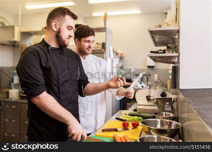 cooking food, profession and people concept - two happy male chefs looking to order or recipe at restaurant kitchen. two chefs cooking food at restaurant kitchen