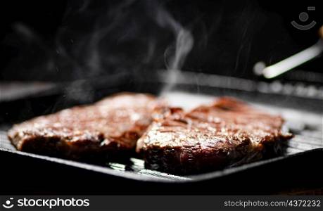 Cooking grilled steak in a frying pan with hot steam. On a black background. High quality photo. Cooking grilled steak in a frying pan with hot steam.
