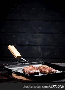 Cooking grilled steak in a frying pan with hot steam. On a black background. High quality photo. Cooking grilled steak in a frying pan with hot steam.