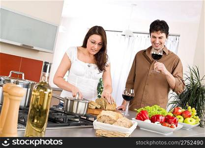 Cooking - happy couple together in modern kitchen drink red wine and cut bread