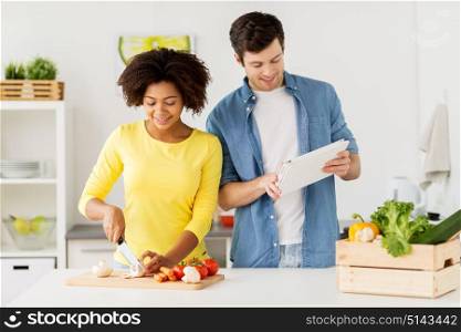 cooking, international and people concept - happy couple with tablet pc computer chopping vegetables at home kitchen. happy couple with tablet pc cooking food at home