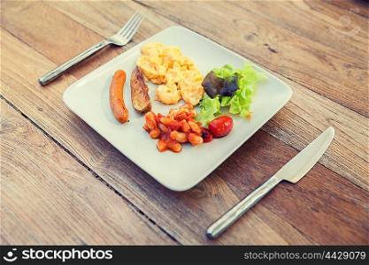 cooking, kitchen and food concept - plate with sausage, eggs, beans and garnish on wooden table at restaurant