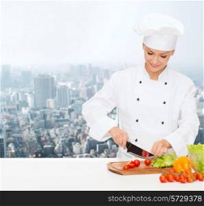 cooking, people and food concept - smiling female chef chopping vegetables over city background