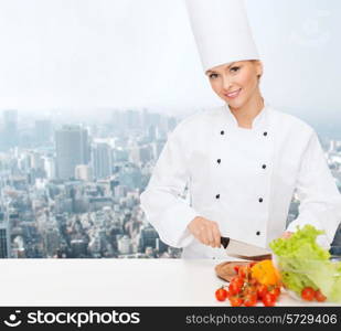 cooking, people and food concept - smiling female chef chopping vegetables over city background