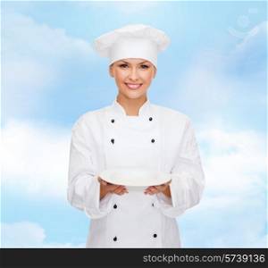 cooking, people and food concept - smiling female chef, cook or baker with empty plate over blue cloudy sky background