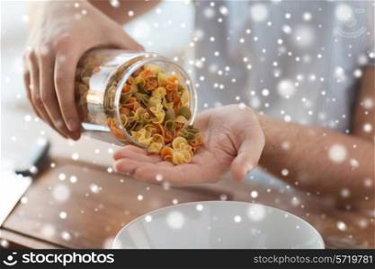 cooking, people and home concept - close up of man emptying jar with colorful pasta in kitchen