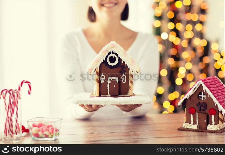 cooking, people, christmas and baking concept - close up of happy woman holding and showing gingerbread house at home