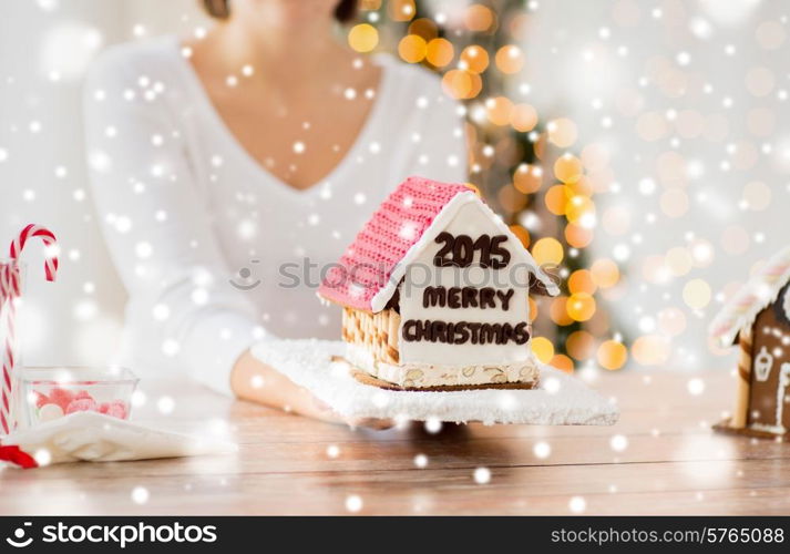 cooking, people, christmas and baking concept - close up of happy woman holding and showing gingerbread house at home