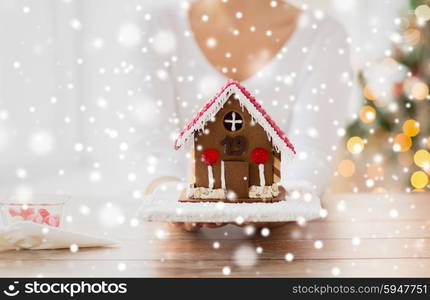 cooking, people, christmas and baking concept - close up of happy woman holding and showing gingerbread house at home