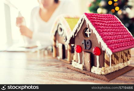 cooking, people, christmas and decoration concept - close up of happy woman making gingerbread houses at home