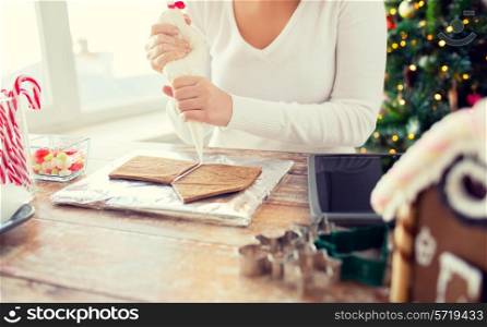 cooking, people, christmas and decoration concept - close up of woman with tablet pc computer making gingerbread houses at home