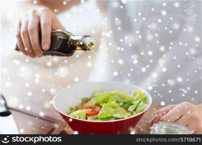 cooking, people, food and home concept - close up of male hands flavoring salad in a bowl with olive oil