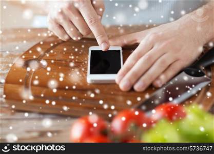 cooking, people, technology and home concept - close up of man reading recipe from smartphone and vegetables on table in kitchen