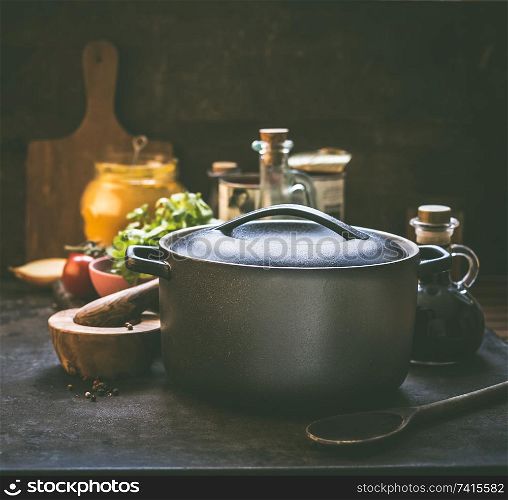 Cooking pot standing on rustic kitchen table with organic ingredients, spices and seasoning. Cast iron cooking pan. Homemade cooking concept