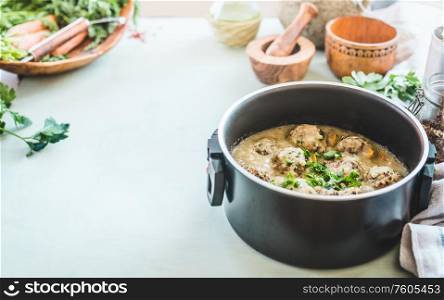 Cooking pot with buckwheat balls in creme sauce standing on kitchen table with herbs and ingredients. Healthy home food cooking