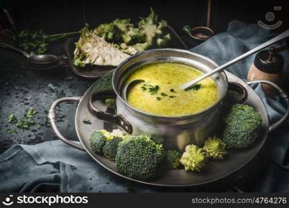 Cooking pot with green romanesco and broccoli soup and ladle on dark rustic kitchen table . Healthy food and diet nutrition concept.