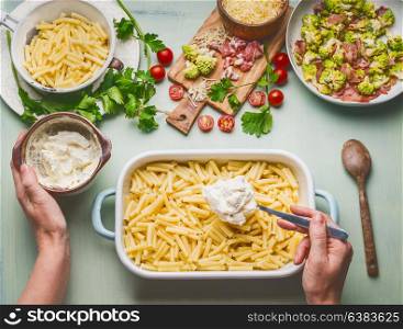 Cooking preparation of American style hearty macaroni pasta in cheesy sauce. Female hand making pasta casserole with tomato, bacon and cheese, top view.