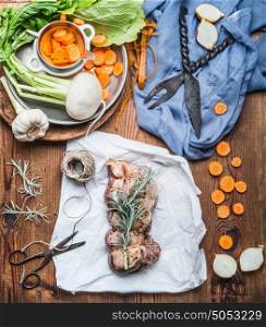 Cooking preparation of raw meat roast with vegetables and fresh condiment on rustic wooden background, top view. Country cuisine