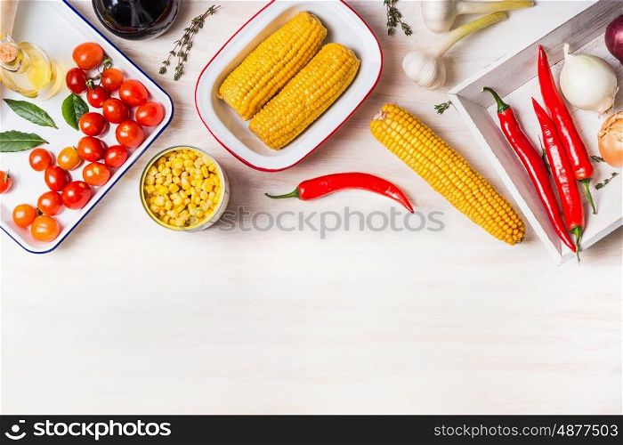 Cooking preparation with ear of corn, canned and cooked corn and ingredients for vegetarian dish on white wooden kitchen table background, top view, border. Healthy food concept
