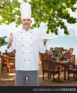 cooking, profession, advertisement and people concept - happy male chef cook holding something on empty plate and showing thumbs up over restaurant lounge on beach