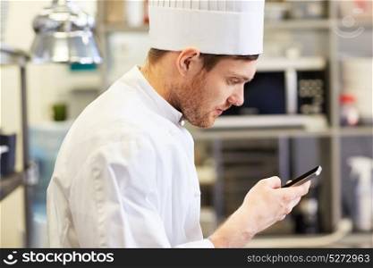 cooking, profession and people concept - close up of male chef cook with smartphone at restaurant kitchen. close up of chef with smartphone at kitchen