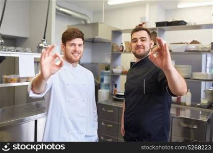 cooking, profession and people concept - happy male chef and cook at restaurant kitchen showing ok hand sign. happy chefs at restaurant kitchen showing ok sign