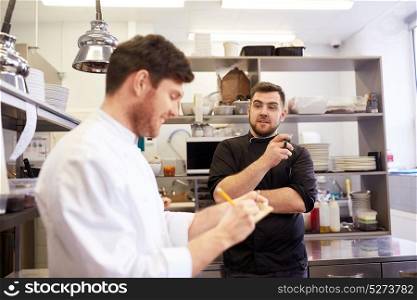 cooking, profession and people concept - happy male chef and cook having coffee break and talking at restaurant kitchen. happy smiling chef and cook at restaurant kitchen