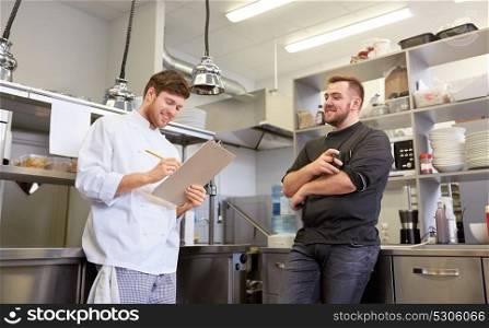 cooking, profession and people concept - happy male chef and cook having coffee break and talking at restaurant kitchen. happy smiling chef and cook at restaurant kitchen