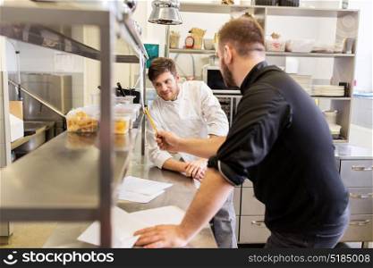 cooking, profession and people concept - happy male chef and cook with grocery lists or bills and food containers at restaurant kitchen. chef and cook with grocery list at kitchen