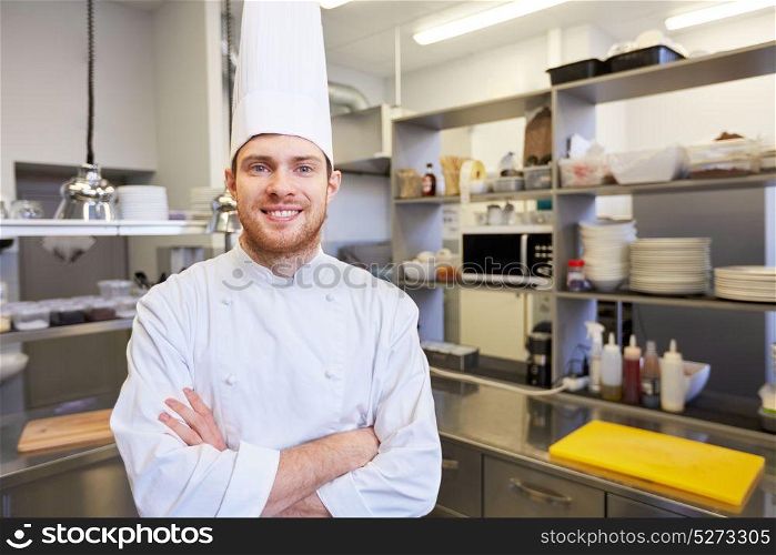 cooking, profession and people concept - happy male chef cook in toque with crossed hands at restaurant kitchen. happy male chef cook at restaurant kitchen