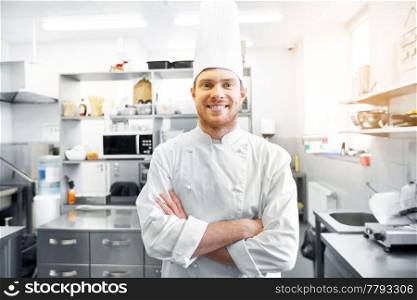 cooking, profession and people concept - happy male chef cook in toque with crossed hands at restaurant kitchen. happy male chef cook at restaurant kitchen