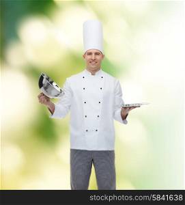 cooking, profession and people concept - happy male chef cook opening cloche cover over green background